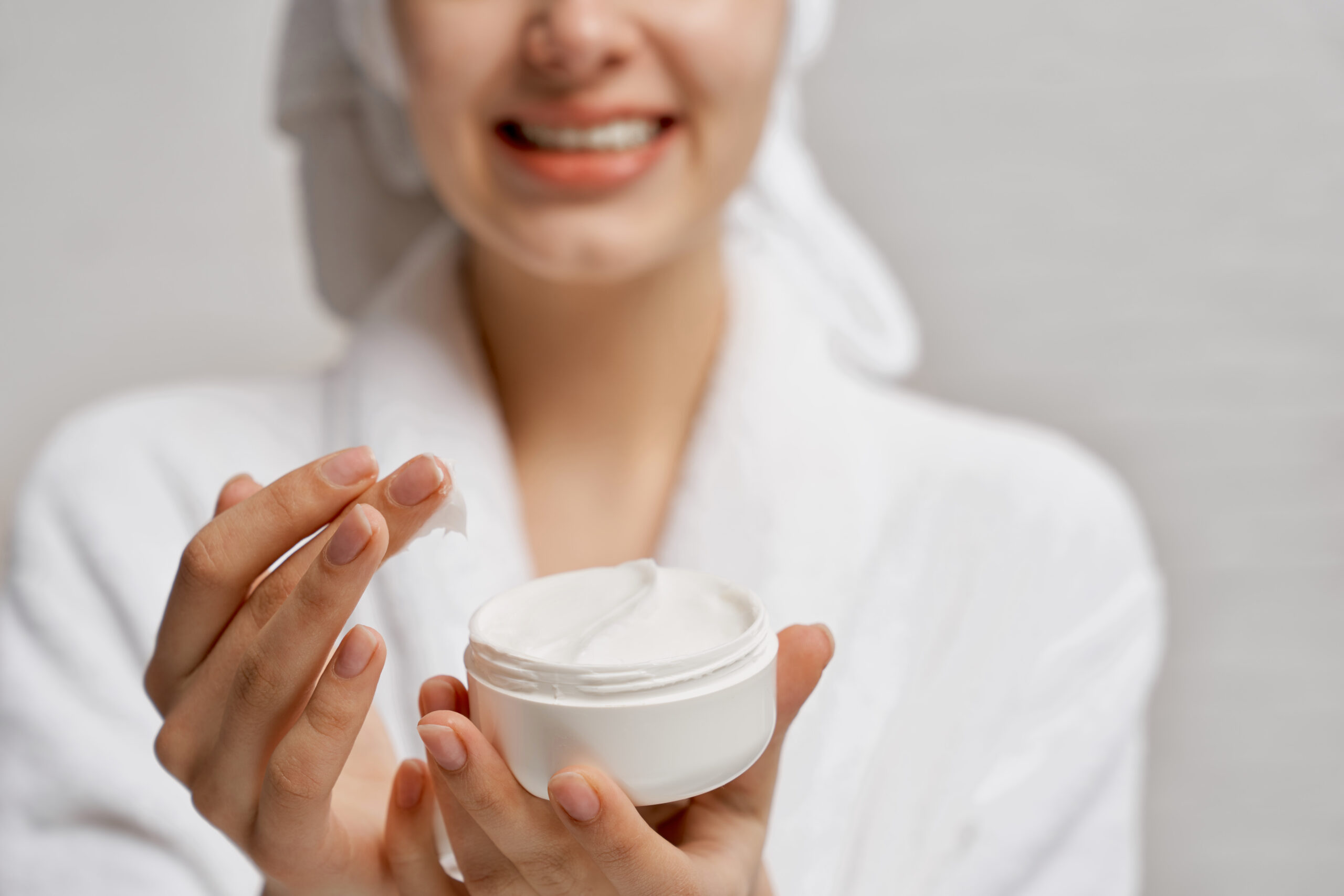 Young woman close up holding moisturizer and demonstrates.